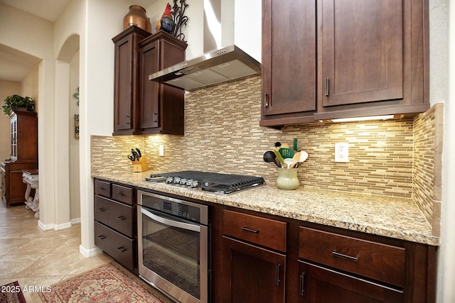 kitchen featuring appliances with stainless steel finishes, tasteful backsplash, light stone counters, and wall chimney exhaust hood