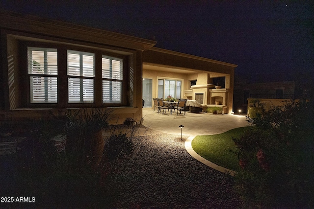 back house at twilight featuring a fireplace and a patio