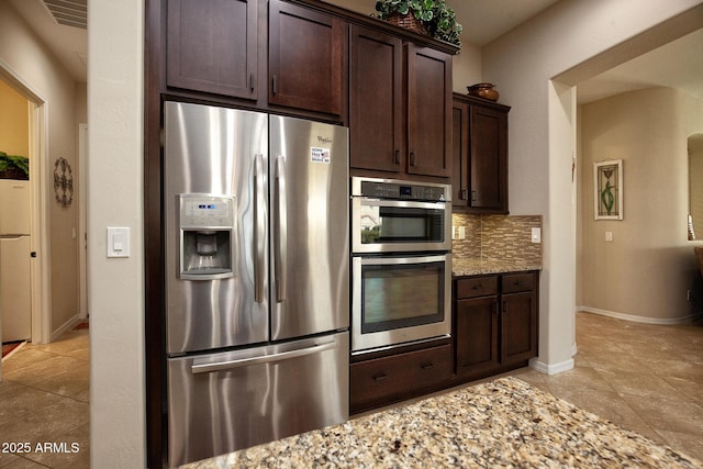 kitchen featuring decorative backsplash, light stone countertops, dark brown cabinets, and stainless steel appliances