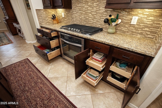 kitchen featuring dark brown cabinetry, light stone counters, decorative backsplash, light tile patterned floors, and appliances with stainless steel finishes