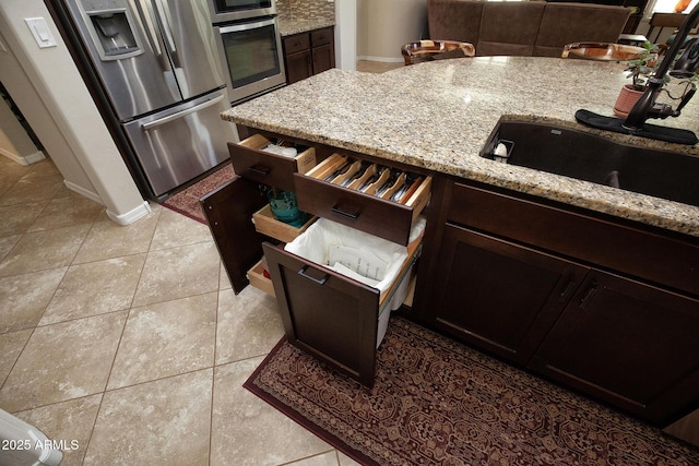 kitchen featuring dark brown cabinetry, light stone counters, light tile patterned flooring, and stainless steel appliances