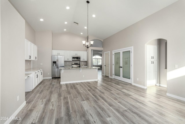 kitchen with a center island with sink, appliances with stainless steel finishes, high vaulted ceiling, white cabinets, and decorative light fixtures