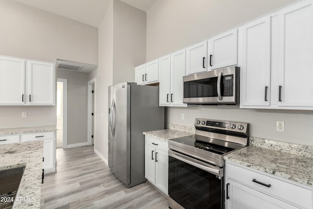 kitchen with a high ceiling, stainless steel appliances, light stone countertops, and white cabinets