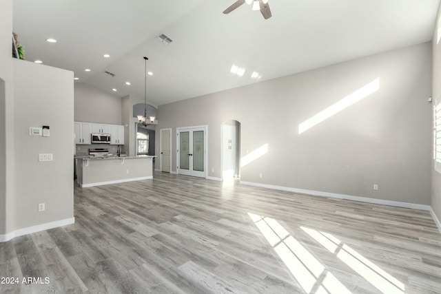 unfurnished living room with ceiling fan with notable chandelier, high vaulted ceiling, and light hardwood / wood-style floors