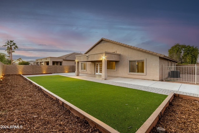 back house at dusk with a balcony, a patio area, and a yard