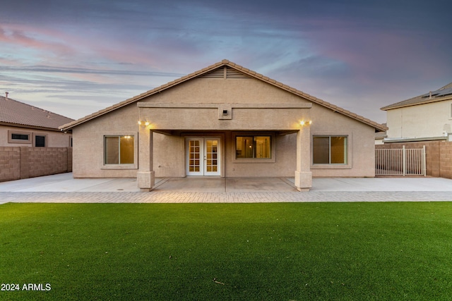 back house at dusk featuring a lawn, french doors, and a patio