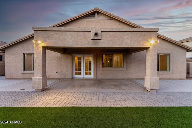 back house at dusk featuring french doors and a patio area