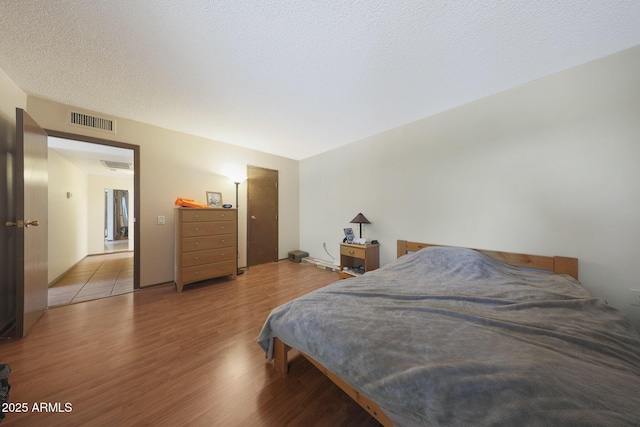 bedroom featuring visible vents, a textured ceiling, and wood finished floors