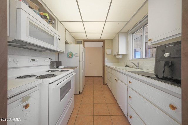 kitchen featuring light tile patterned floors, light countertops, white cabinets, a sink, and white appliances