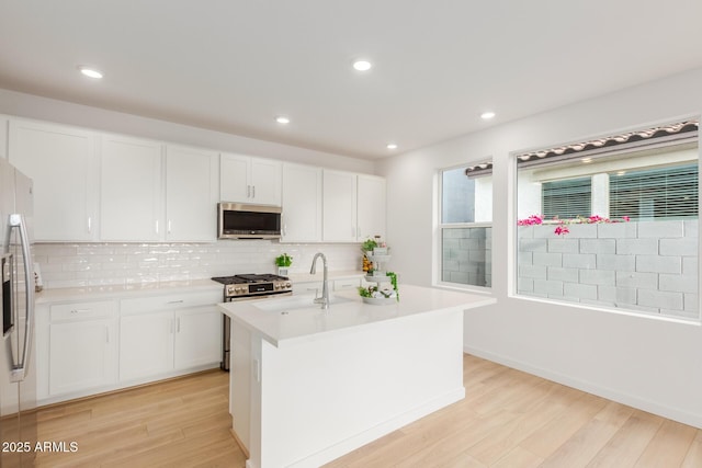 kitchen featuring tasteful backsplash, light countertops, appliances with stainless steel finishes, light wood-style floors, and a sink