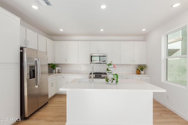 kitchen featuring stainless steel appliances, backsplash, visible vents, and light wood-style floors