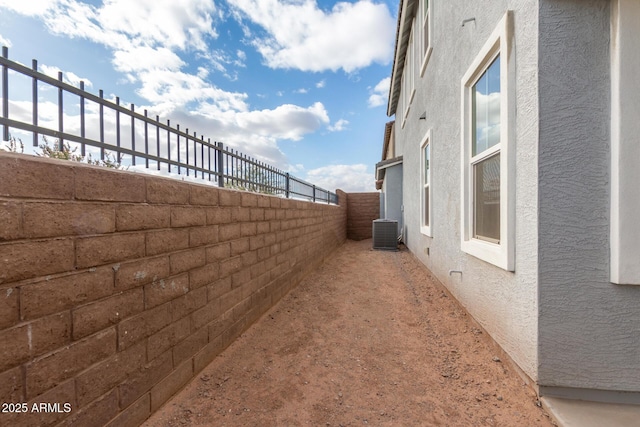 view of side of home featuring a fenced backyard, central AC unit, and stucco siding