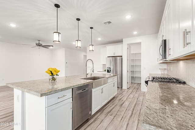 kitchen with white cabinets, appliances with stainless steel finishes, decorative light fixtures, sink, and a kitchen island with sink