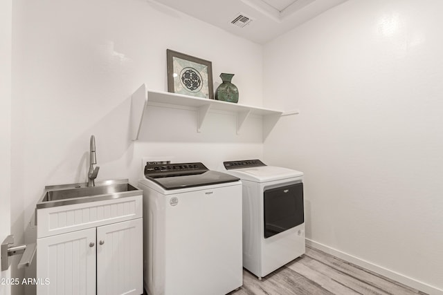 laundry area featuring sink, independent washer and dryer, cabinets, and light hardwood / wood-style floors