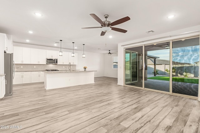 kitchen with white cabinetry, hanging light fixtures, stainless steel appliances, and an island with sink