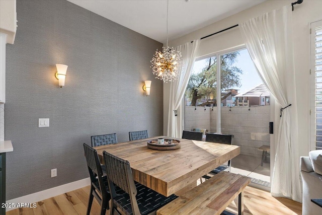 dining room with an inviting chandelier, light wood-style flooring, wallpapered walls, and baseboards