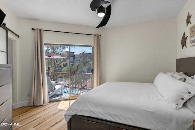 bedroom with access to exterior, baseboards, ceiling fan, a barn door, and light wood-style flooring