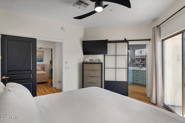 bedroom featuring visible vents, ceiling fan, a sink, light wood-style floors, and a barn door