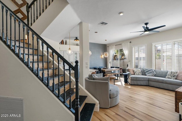 living room featuring visible vents, stairway, wood finished floors, and ceiling fan with notable chandelier