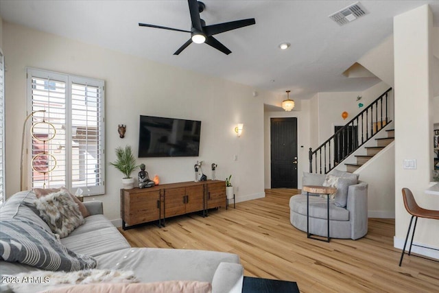 living area with wood finished floors, baseboards, visible vents, ceiling fan, and stairs