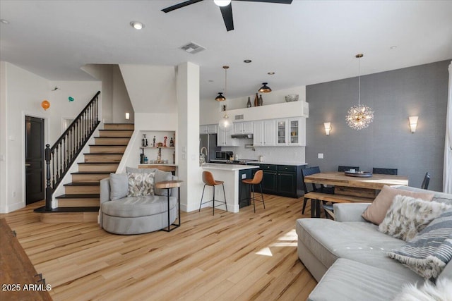 living area with light wood-type flooring, ceiling fan with notable chandelier, visible vents, and stairway