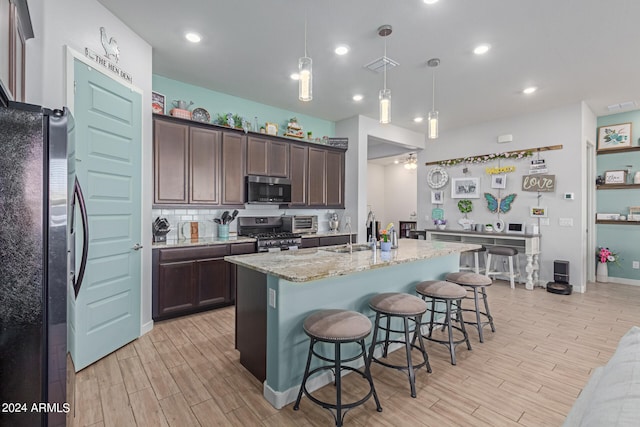 kitchen featuring hanging light fixtures, stainless steel appliances, light hardwood / wood-style floors, sink, and a kitchen breakfast bar