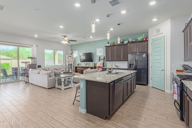 kitchen featuring appliances with stainless steel finishes, sink, ceiling fan, light stone counters, and light wood-type flooring