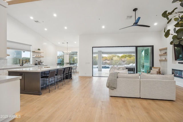 living room featuring high vaulted ceiling, sink, ceiling fan with notable chandelier, and light hardwood / wood-style floors