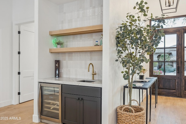 bar with backsplash, beverage cooler, sink, and light wood-type flooring