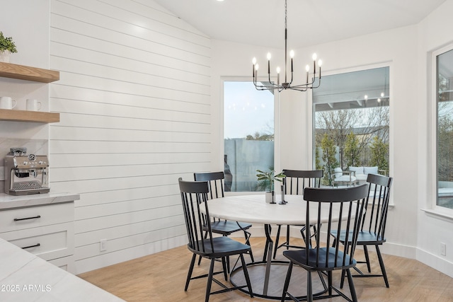 dining room with lofted ceiling, a chandelier, light hardwood / wood-style floors, and wood walls