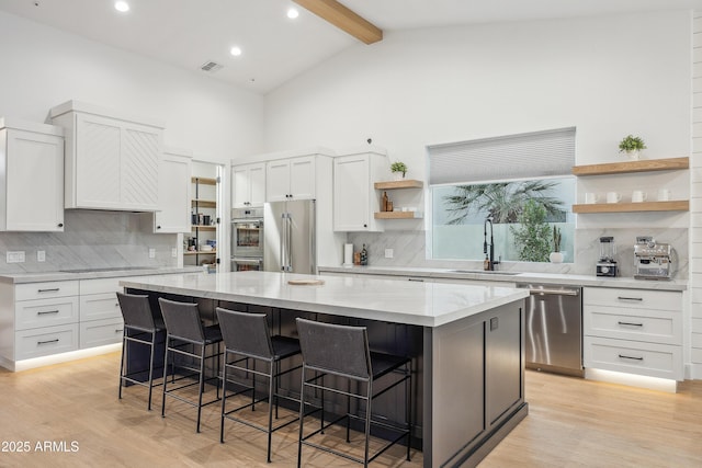 kitchen with white cabinetry, a center island, a kitchen breakfast bar, beamed ceiling, and stainless steel appliances