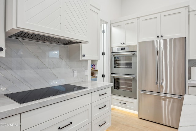 kitchen with white cabinetry, stainless steel appliances, light stone counters, decorative backsplash, and custom exhaust hood