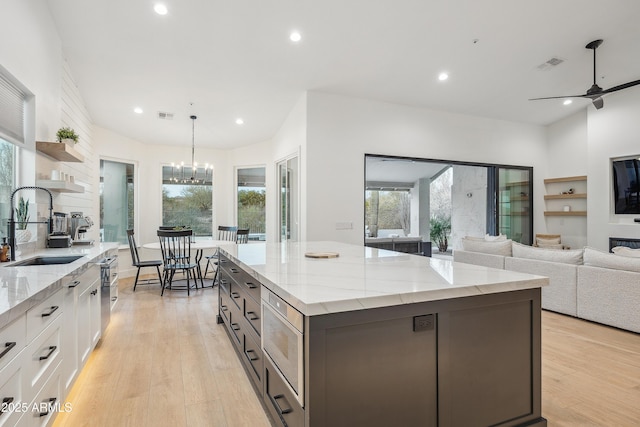 kitchen with sink, light stone counters, stainless steel microwave, light hardwood / wood-style floors, and white cabinets