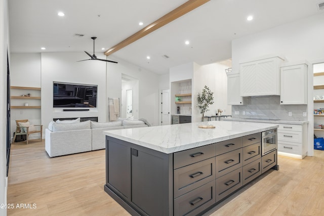 kitchen featuring white cabinetry, vaulted ceiling with beams, a center island, light stone counters, and light wood-type flooring