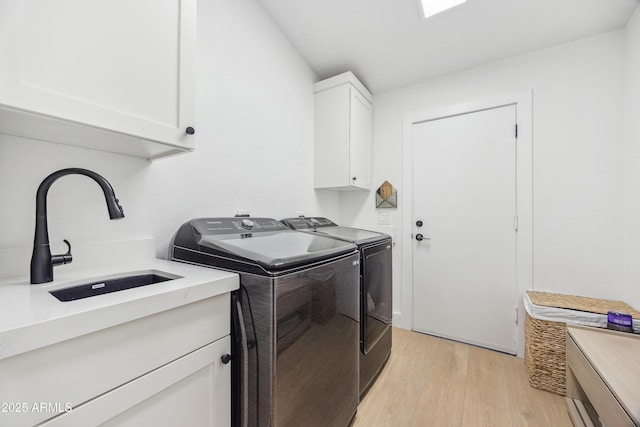 clothes washing area with independent washer and dryer, sink, light hardwood / wood-style flooring, and cabinets