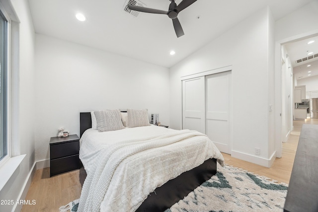 bedroom featuring lofted ceiling, light hardwood / wood-style flooring, stainless steel fridge, and a closet