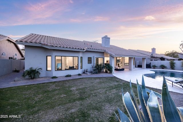 back house at dusk with a fenced in pool, a patio, and a yard