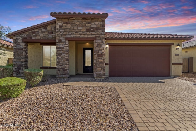 view of front of home featuring stone siding, decorative driveway, an attached garage, a tile roof, and stucco siding