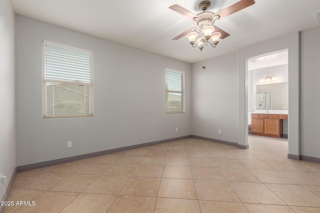 interior space featuring baseboards, a ceiling fan, ensuite bathroom, and light tile patterned floors