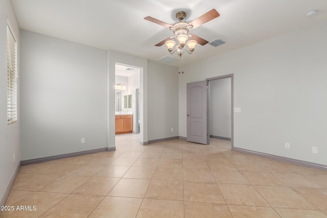 unfurnished bedroom with light tile patterned floors, baseboards, ensuite bath, visible vents, and a ceiling fan