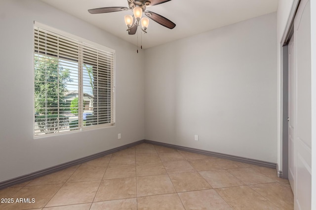 empty room with a ceiling fan, light tile patterned floors, and baseboards