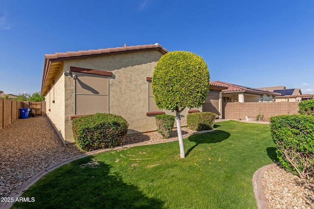 exterior space featuring a fenced backyard, a tile roof, stucco siding, and a yard