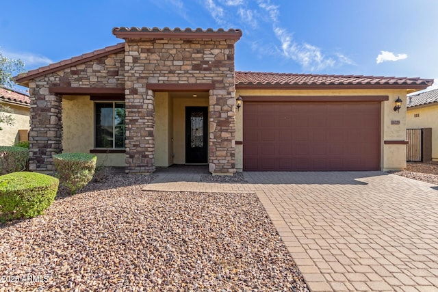 mediterranean / spanish-style house featuring stucco siding, stone siding, a tiled roof, decorative driveway, and a garage
