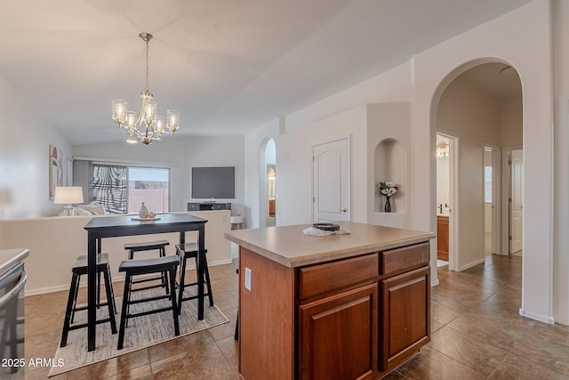 kitchen with arched walkways, open floor plan, a kitchen island, a chandelier, and decorative light fixtures