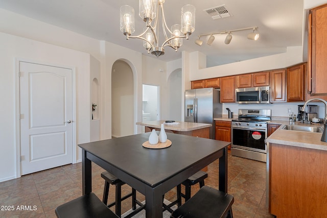 kitchen featuring appliances with stainless steel finishes, a sink, arched walkways, brown cabinets, and light countertops