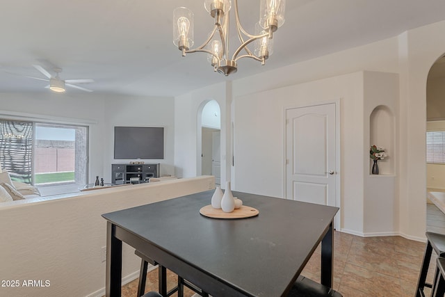 dining space with arched walkways, a ceiling fan, a chandelier, and baseboards