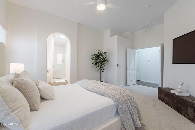 carpeted bedroom with arched walkways, connected bathroom, and a ceiling fan