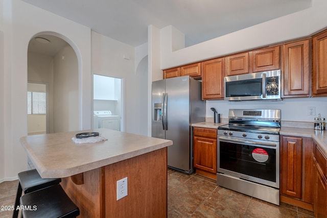 kitchen with stainless steel appliances, washer and clothes dryer, arched walkways, and brown cabinets