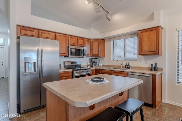kitchen featuring stainless steel appliances, a sink, brown cabinets, a kitchen bar, and a center island