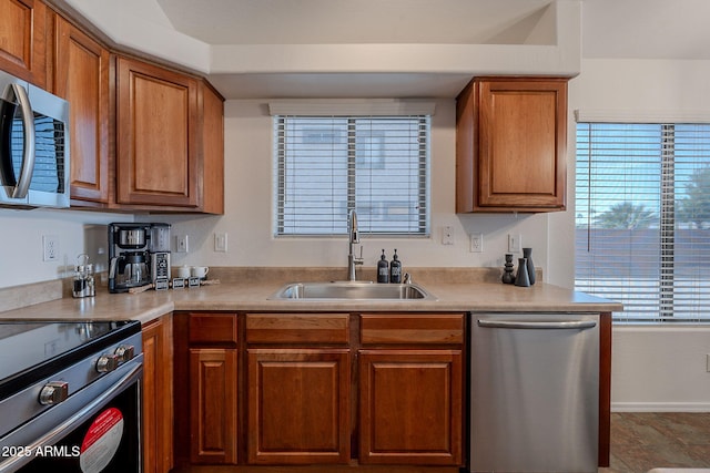 kitchen with appliances with stainless steel finishes, a sink, brown cabinets, and light countertops
